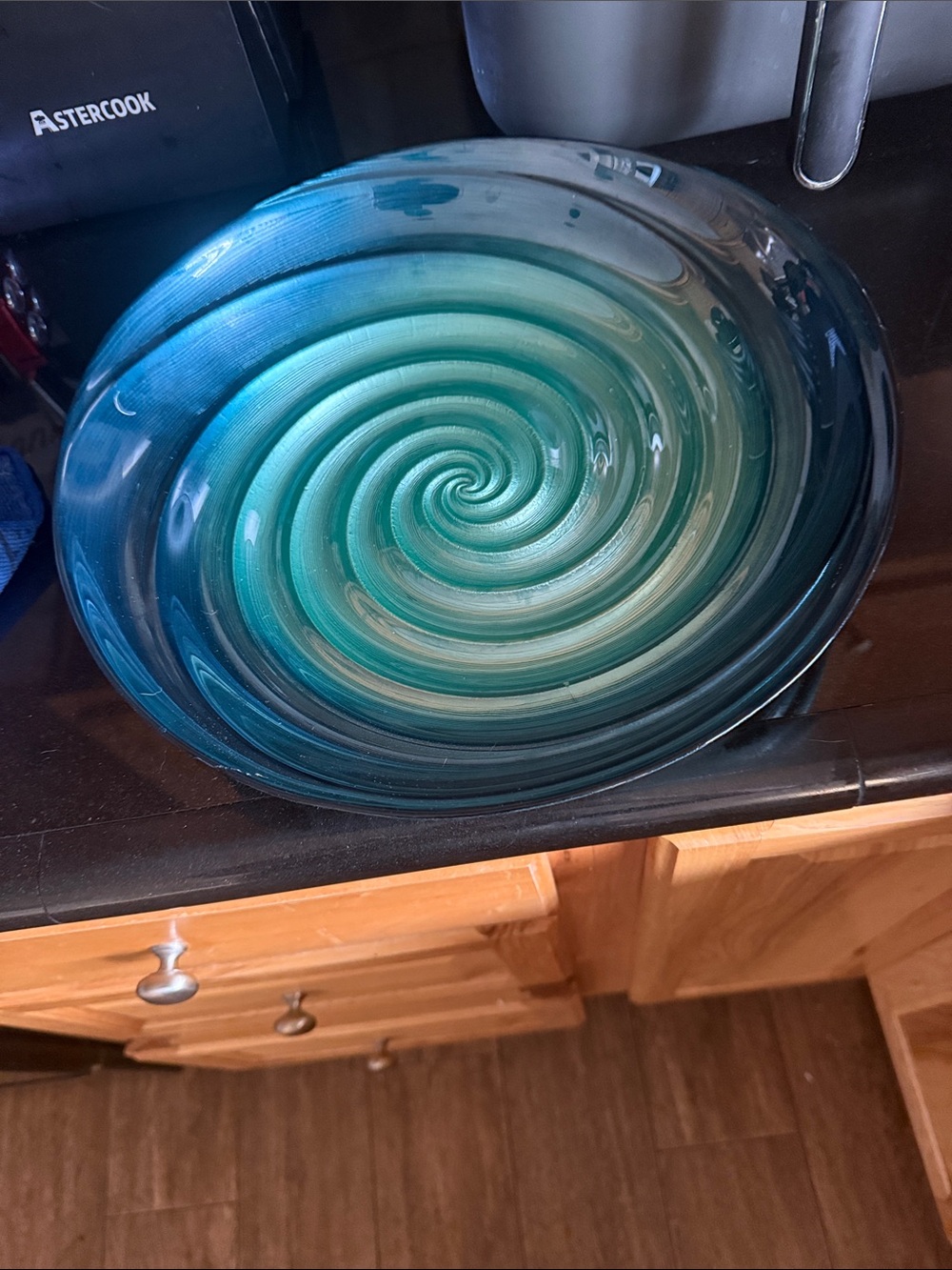 An Orren Ellis blue-green glass charger with a swirl design.